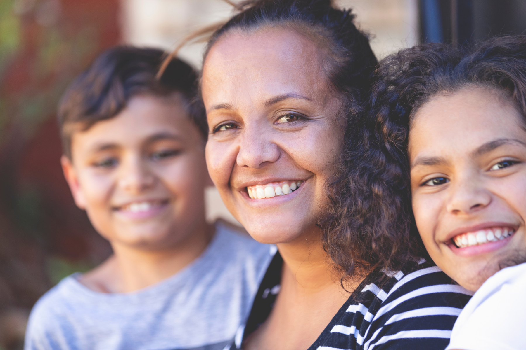 An Aboriginal woman with two children. All are smiling.