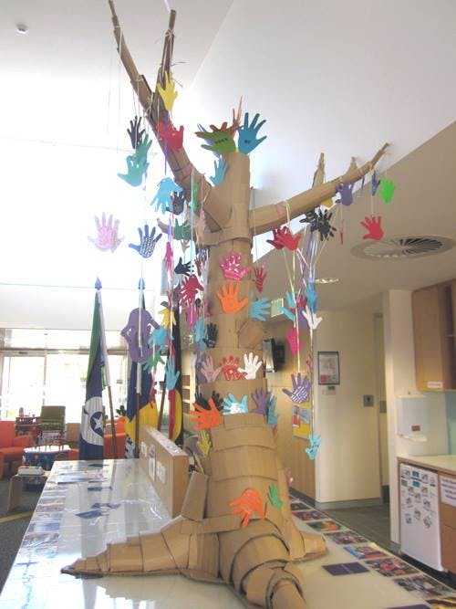 A tree made out of cardboard with colured hands hanging from each branch. The tree is sitting on table inside the West Belconnen Child & Family Centre.