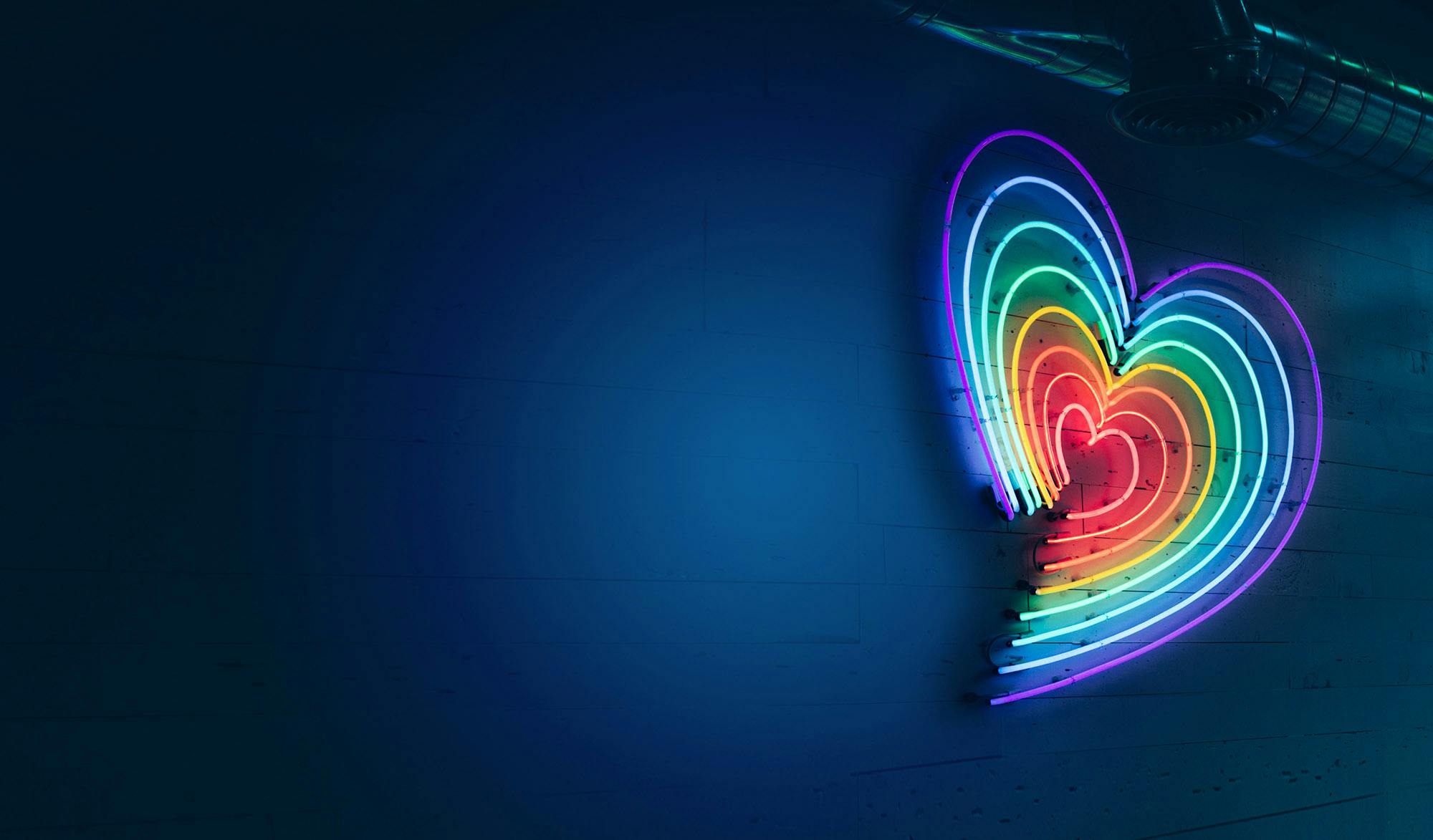 A rainbow coloured neon light in the shape of a heart