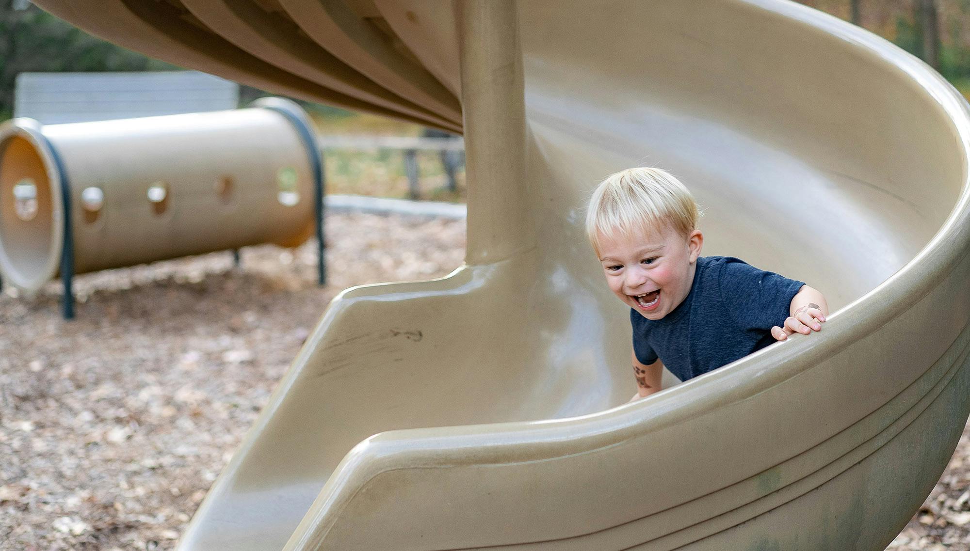 A young boy smiling happily on a slide.