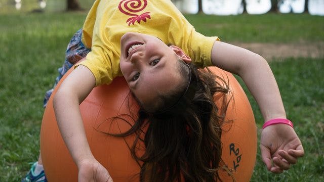 A young girl smiling while lay backwards over an exercise ball