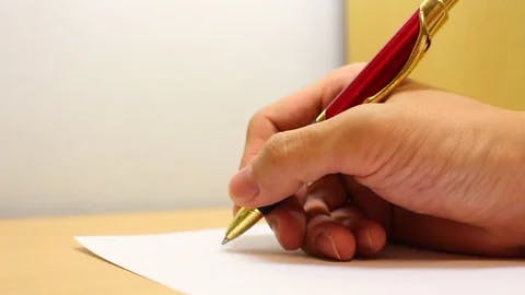 a hand holds a pen above a blank sheet of paper, about to write
