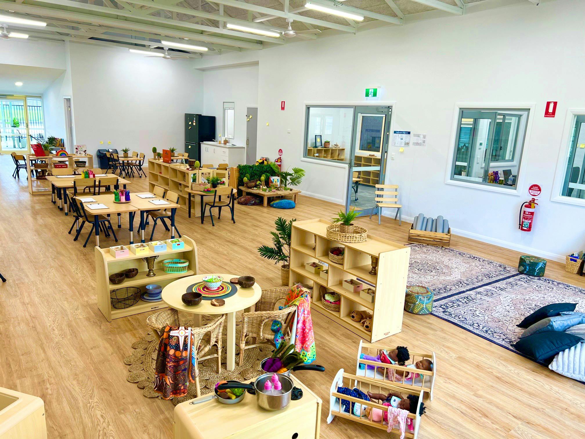 Image of a large room filled with children's tables and shelving, with play equipment throughout.