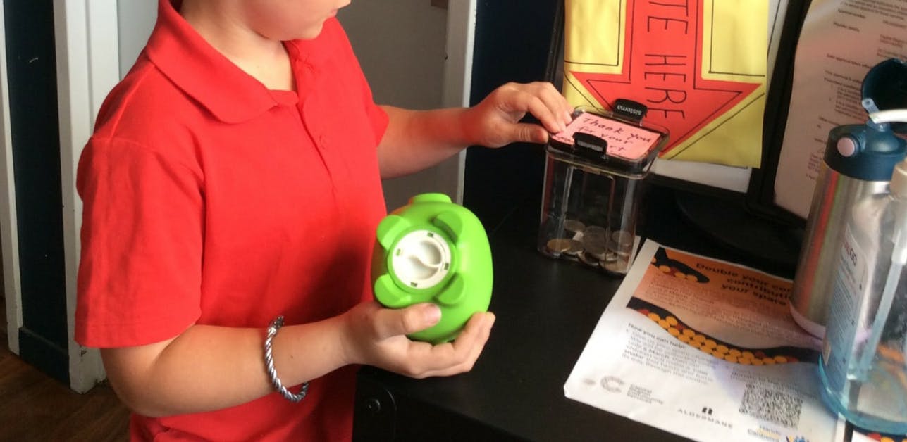A child, donating coins from his piggy bank into the donation box.