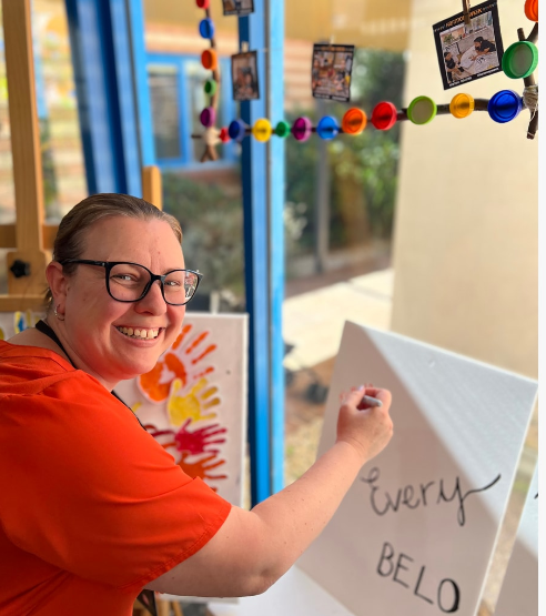 A photo of CRCS team member Mel, writing a message on a our 'Everyone belongs' canvas.