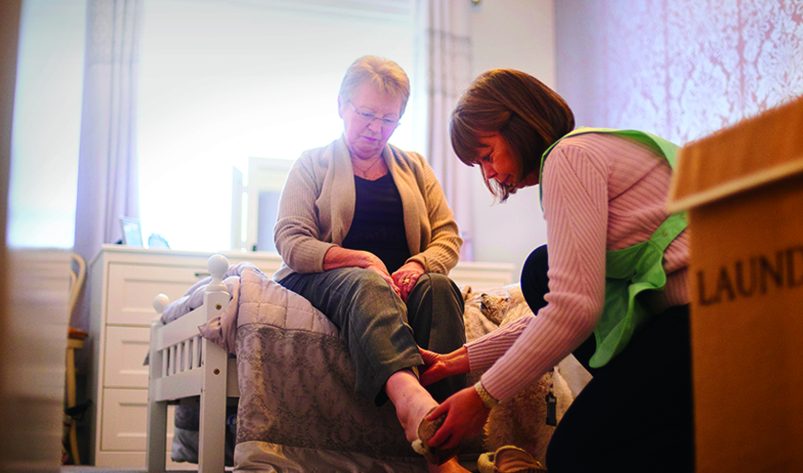 A aged care worker helping an old lady put her shoes on.