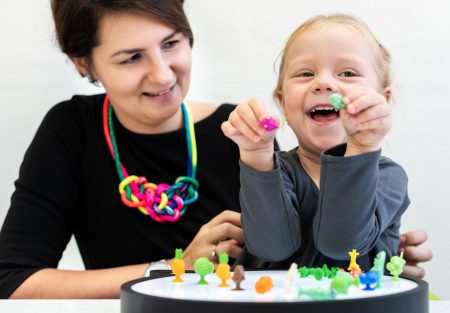 Toddler girl in child occupational therapy session doing sensory playful exercises with her therapist.