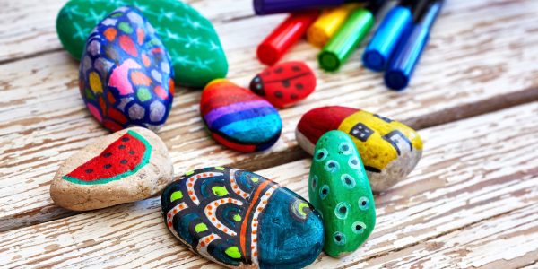 Hand-painted colorful stones and acrylic pens on a vintage textured wooden table. Stone painting.