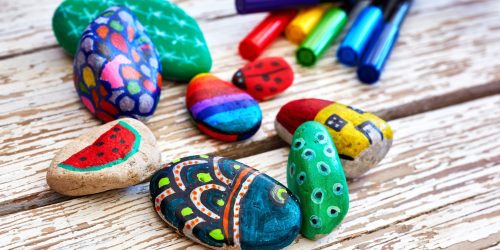 Hand-painted colorful stones and pens Hand-painted colorful stones and acrylic pens on a vintage textured wooden table. Stone painting.