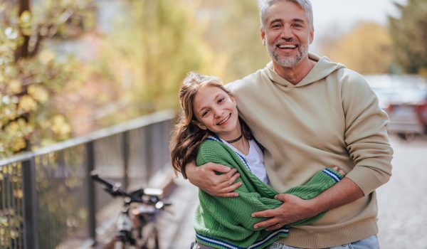 A teenage daughter hugging her father outside in town when spenidng time together.