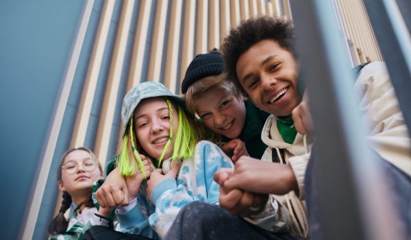 Portrait of happy close teenage friends smiling at camera while sitting on steps outdoors and embracing each other
